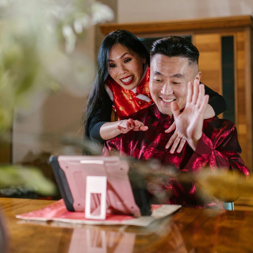 Joyful couple in traditional outfits video calling on a tablet indoors.